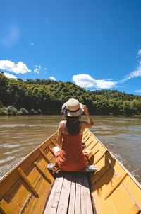 Rear view of young woman sitting in boat on lake against blue sky