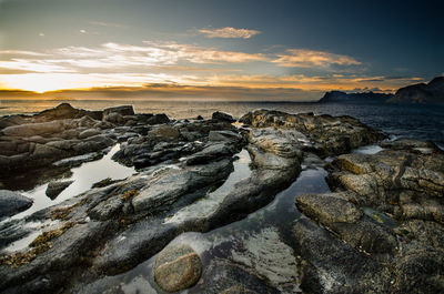 Rocks on beach against sky during sunset