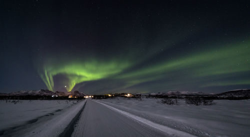 Empty snow covered road against aurora borealis at night