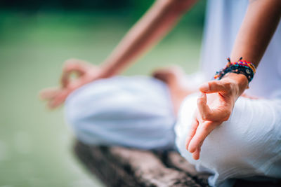 Midsection of woman doing yoga while sitting on pier at lake