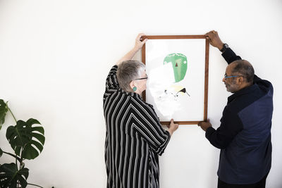 Heterosexual couple looking at each other while hanging painting on wall