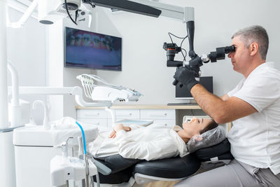 Dentist using dental microscope treating patient teeth at dental clinic office. medicine, dentistry