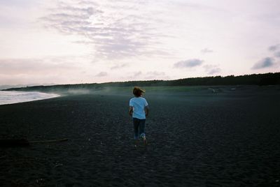 Rear view of man standing on beach against sky