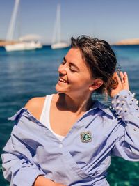 Smiling young woman sitting against sea during sunny day