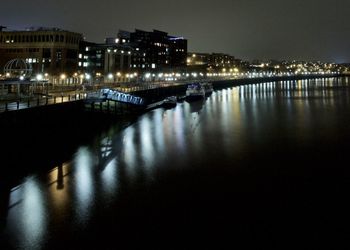 Illuminated buildings by river against sky at night