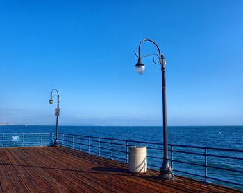 Street light by sea against clear blue sky