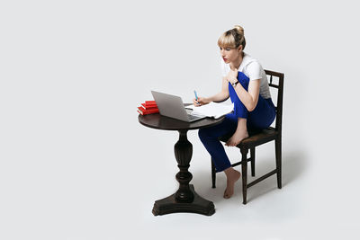 Portrait of smiling young woman using laptop while sitting against white background