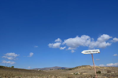 Road sign by landscape against blue sky