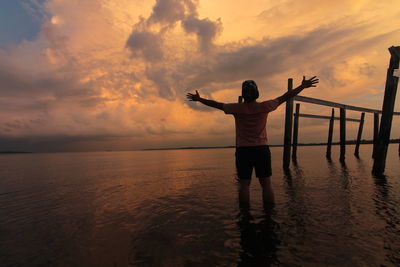 Full length of silhouette person standing in sea against sky during sunset