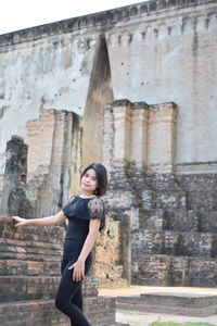 Portrait of young woman standing by old building