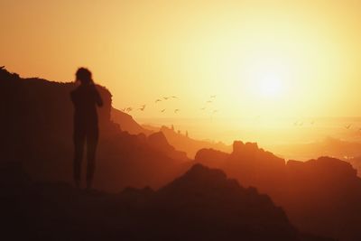 Full length rear view of silhouette woman standing by mountains against clear sky during sunset