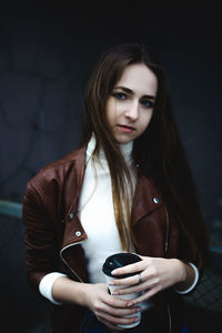 Portrait of beautiful young woman holding coffee cup while standing outdoors