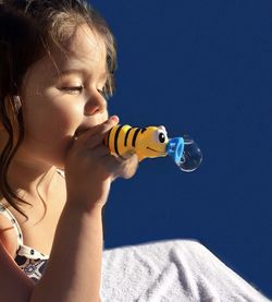 Close-up of girl blowing bubble against blue background