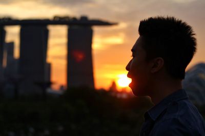 Optical illusion of boy eating sun against sky during sunset at marina bay sands