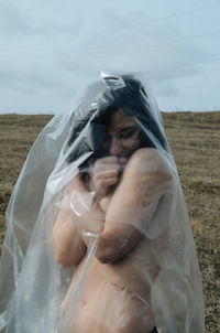 Shirtless young woman covered with plastic standing on land