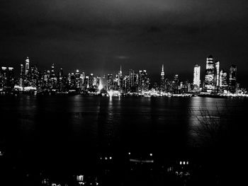 Illuminated buildings by river against sky at night