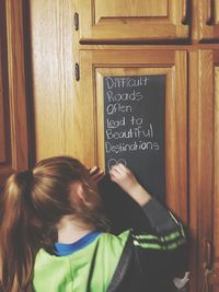 Rear view of girl writing with chalk on door