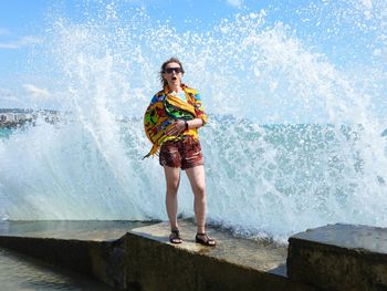 Full length of young woman standing by waves 