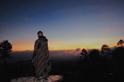 Silhouette man standing by trees against sky during sunset