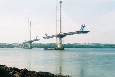 Incomplete suspension bridge over sea against sky