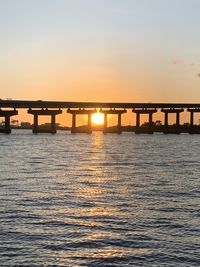 Silhouette bridge over sea against sky during sunset