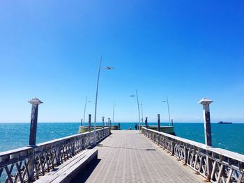 Pier on sea against clear blue sky