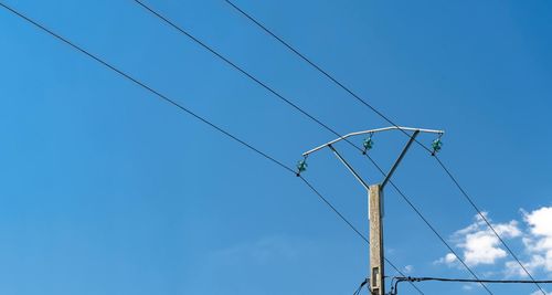 Low angle view of electricity pylon against blue sky