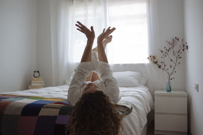 Curly-haired woman lying in bed playing with her hands.