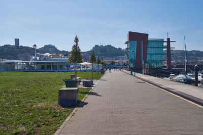 Empty footpath amidst buildings in city against sky