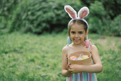 Girl with eggs basket and bunny ears on easter egg hunt in garden.