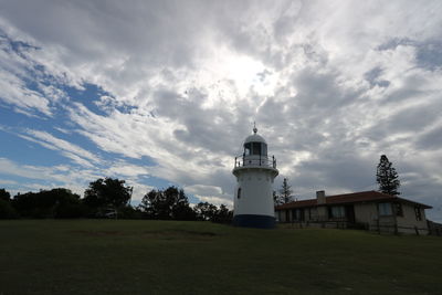 Lighthouse on field by building against sky