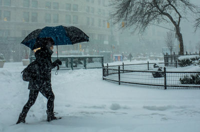 Side view of man with umbrella walking on snowy street during snowfall