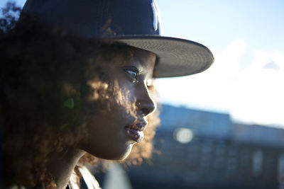 Close-up of woman in cap looking away while standing against sky