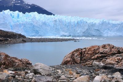 Scenic view of glacier by mountain against sky