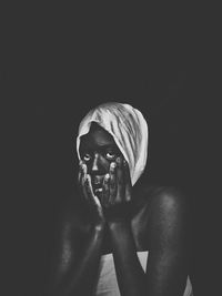 Portrait of young woman touching face while sitting against black background