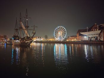 Illuminated ferris wheel by sea against sky at night