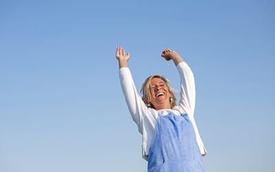 Rear view of woman with arms raised standing against clear sky