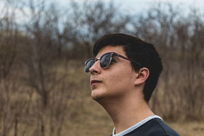 Young man looking away while wearing sunglasses against trees