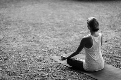 Rear view of young woman meditating in lotus position at park