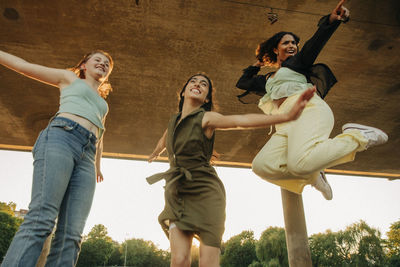 Low angle view of happy teenage girls jumping under bridge