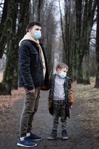 Full length of father and son wearing mask standing in forest