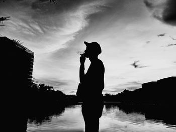 Silhouette man standing by lake against sky during sunset