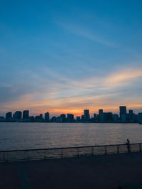 City by sea against sky at sunset