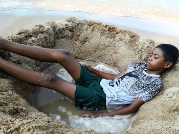 High angle view of boy lying in pit at beach