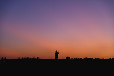 Silhouette of a person standing on a field against sky during sunset