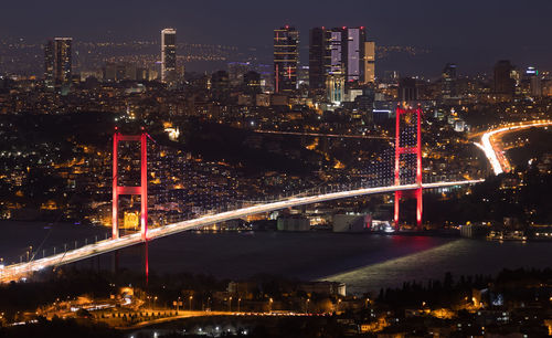 Illuminated bridge and buildings against sky at night