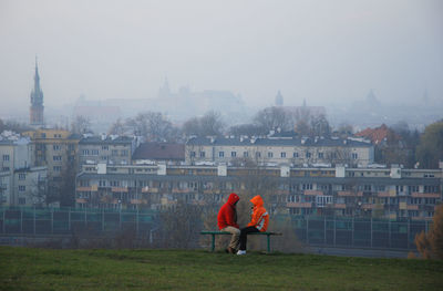 Friends sitting face to face against buildings during foggy weather