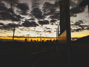 Road by silhouette city against sky during sunset