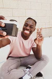 Smiling man taking selfie with camera against wall