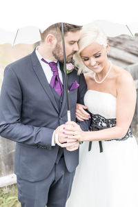 Smiling bride and groom standing with umbrella